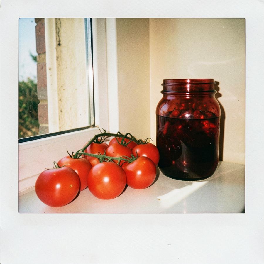 Ripe red tomatoes ripening on a sunlit windowsill beside a glass jar